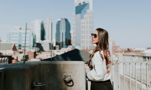 woman with sunglasses stands on a rooftop overlooking the city